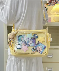 Detailed view of yellow canvas ita bag with a clear window displaying anime pins and cards