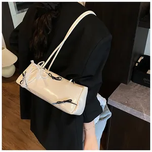 Detail of off-white baguette bag with pearl chain and bow accents on model's shoulder