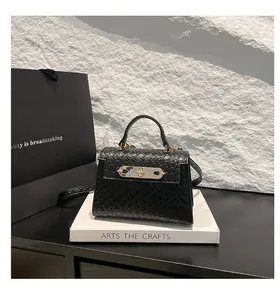 Detail of black woven texture handbag with gold metal clasp on white display pedestal