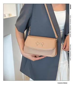 Detail of beige leather shoulder bag featuring a gold bow clasp on neutral background
