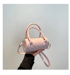 Close-up of pink cylindrical crossbody bag with white polka dots and dual handles