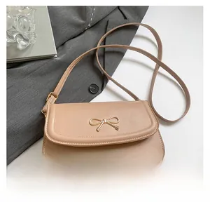 Detail of beige shoulder bag with a gold bow clasp on a minimalist business background