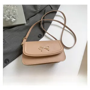 Detail of minimalist beige shoulder bag featuring a decorative golden bow clasp closure