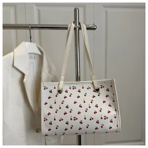 Détails d'un sac cabas blanc avec imprimés cerises et œillets métalliques dorés élégants