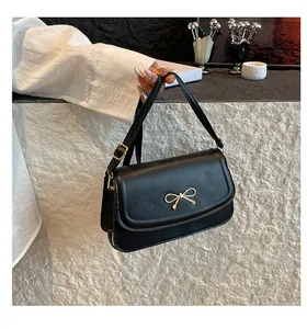 Detail of black PU leather shoulder bag featuring a gold metal bow and adjustable strap