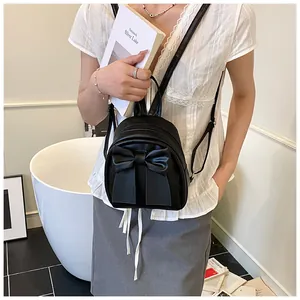 Detail of a black mini backpack with a large bow showing matte leather and adjustable straps