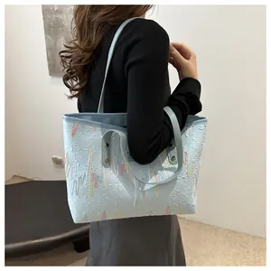 Detalle de bolso tote azul claro con texturas grabadas y bordados ondulados de colores