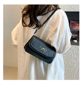 Detail of black leather crossbody bag with golden bow buckle on a white shirt model