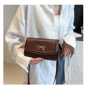 Detail of dark brown leather handbag featuring a golden metal bow on the front flap