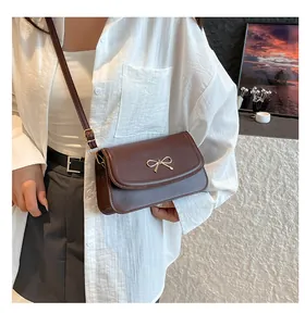 Close-up of a brown underarm bag with a golden metal bow and elegant leather strap