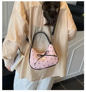 Sac à bandoulière plissé rose avec nœud noir et pendentif cœur porté par un mannequin
