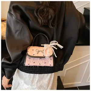 Detail of pink pleated crossbody bag with lace bow charm and pearl strap on model
