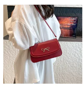 Close-up of red leather handbag featuring a stylish gold metal bow clasp on the flap