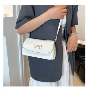 Detailed view of white faux leather bag with elegant golden bow buckle and fine strap