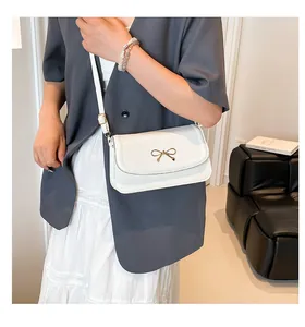 Detail of white PU leather crossbody bag featuring a decorative gold metal bow on the front