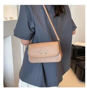 Detail view of beige shoulder bag with gold bow clasp on a grey suit jacket