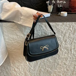 Elegant black PU leather underarm bag with a golden metal bow and adjustable strap
