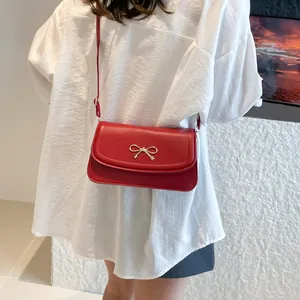 Minimalist red leather shoulder bag with a silver bow buckle shown on a model