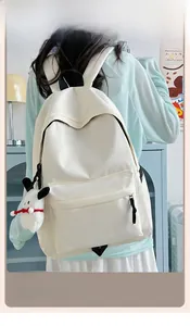 Rear view of cream white nylon backpack with cute plush charm on a female model