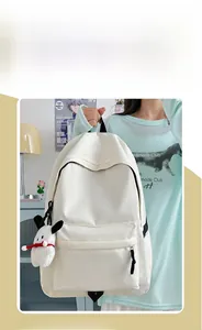 Detail view of a white nylon school backpack with a cute puppy plush charm pendant