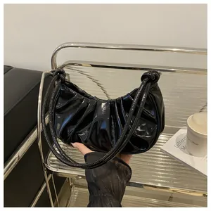 Detail of glossy pleated black underarm bag with thin shoulder straps and knot design