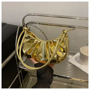 Detail of a metallic gold pleated shoulder bag with knotted handle and ruched texture