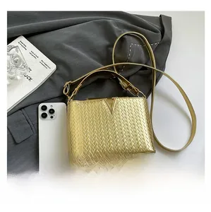 Detalle de bolso dorado con textura trenzada, hebilla de metal en V y teléfono para comparar tamaño