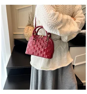 Detail of burgundy shell bag featuring 3D checkered texture and gold metal zippers