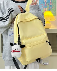 Detail view of a pale yellow nylon backpack with a cute plush puppy charm accessory