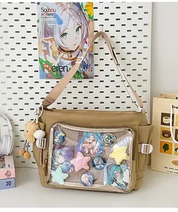 Detail view of khaki canvas ita bag featuring a large clear PVC window with anime badges