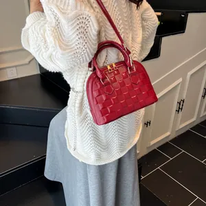 Detail of red shell-shaped handbag with woven texture and gold hardware worn by model