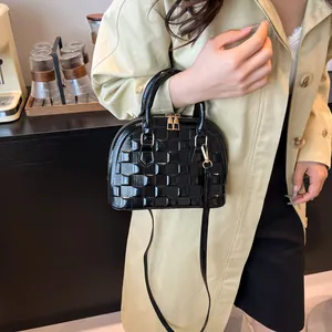 Close-up of black glossy patent leather shell bag with textured woven pattern and strap