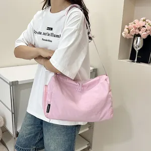 Détail du sac bandoulière rose en nylon imperméable avec étiquette de marque porté par modèle