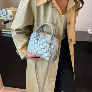 Close-up of a silver shell bag with grid texture, gold hardware and adjustable strap