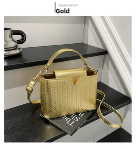 Detalle de bolso bandolera trenzado dorado con cierre en V y elegante asa superior