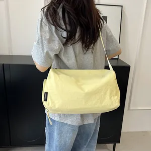 Détail d'un sac bandoulière en nylon jaune clair avec étiquette tissée et texture froissée