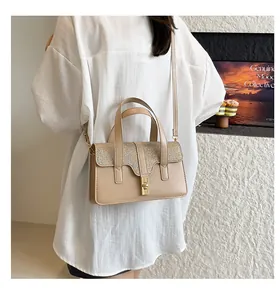 Sac à main beige élégant à motif crocodile avec détails dorés porté par un mannequin