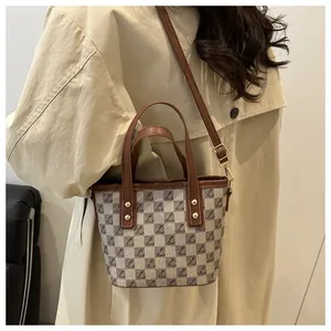 Detail of checkered bucket bag with gold hardware on a beige trench coat model