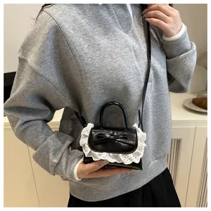 Détail du mini sac à main noir avec bordure en dentelle blanche et nœud élégant