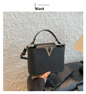 Detalle de bolso bucket negro con textura trenzada y logotipo metálico dorado en V