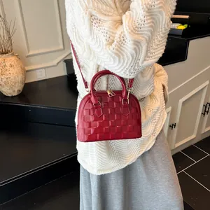 Glossy red shell bag with checkered pattern being carried by a model in interior setting