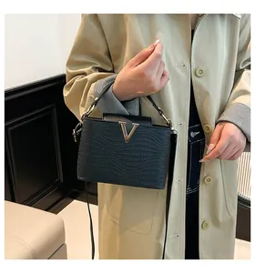 Détail d'un sac à main noir tressé avec boucle métallique en V doré et bandoulière