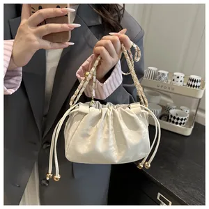 Detail of cream drawstring bucket bag with gold chain strap and metal bead accents