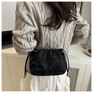 Detail of a black pleated chain bag featuring golden sphere accents and a drawstring closure
