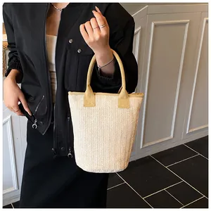 Macro shot of the beige herringbone straw texture and tan fabric handle of the tote bag