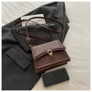 Detailansicht der kaffeebraunen Ledertasche mit Goldschließe auf einem grauen Sakko