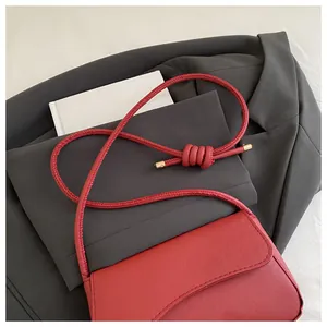 Detail van rode baguette tas met geknoopte touwriem en goudkleurige hardware
