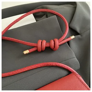 Detail van rode leren tas met textuur, geknoopte schouderband en gouden metalen accenten