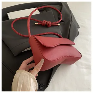Detail van rode leren baguette tas met gegolfde bodem op een zwart jasje