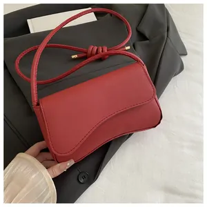 Detail van rode baguette tas met gegolfde flap en geknoopte riem op een zwart pak